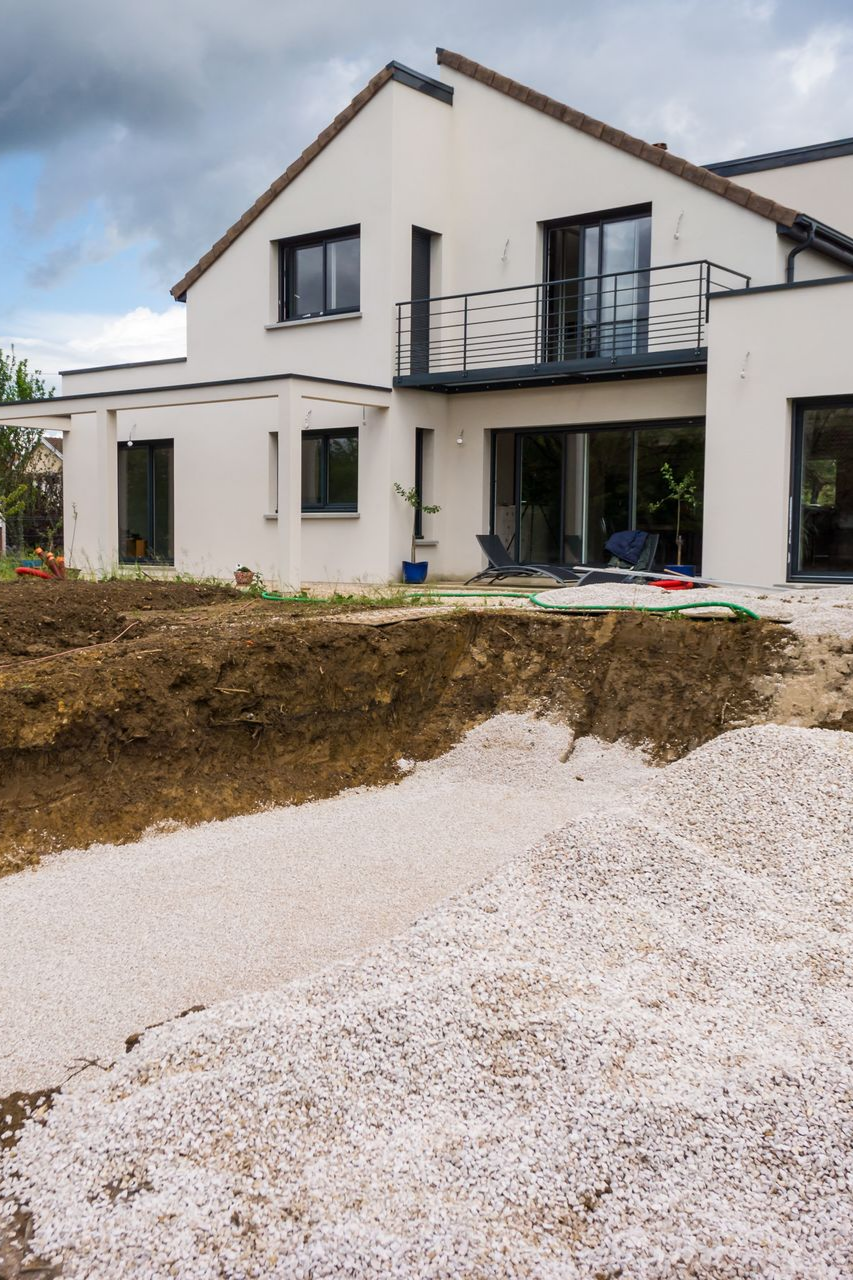 Vue extérieure d'une maison à deux étages en construction ; gravier et terre au premier plan.