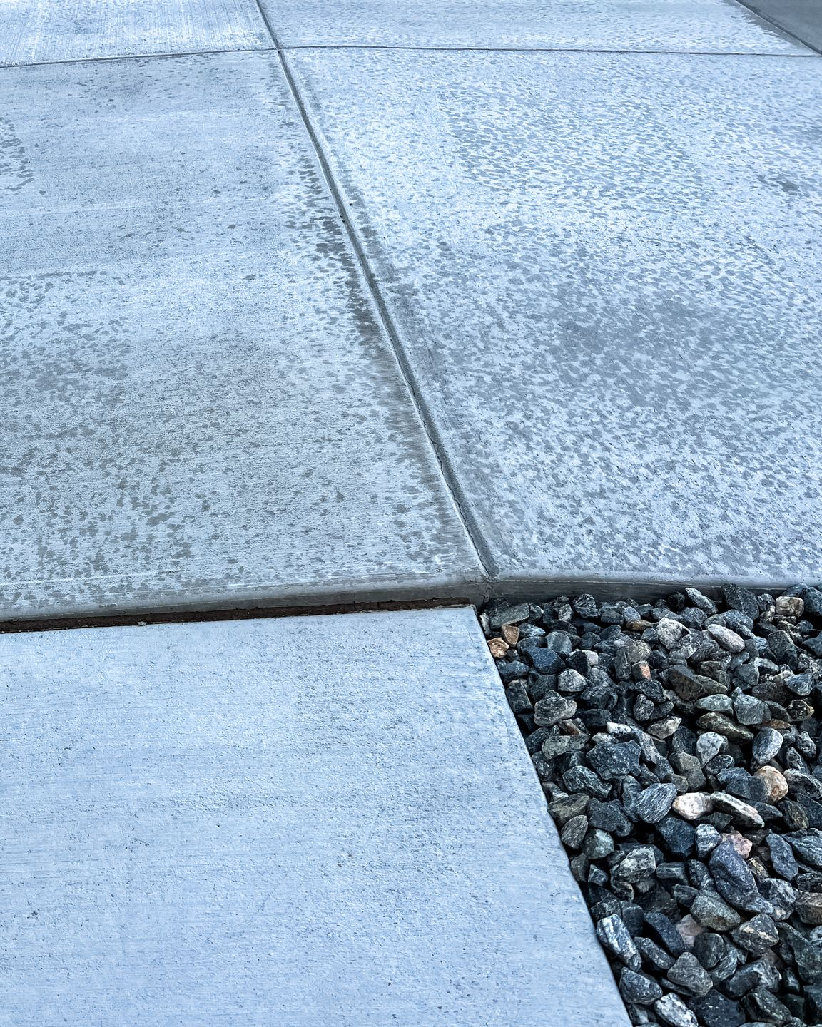 Trottoir en béton gris avec une section de gravier foncé.