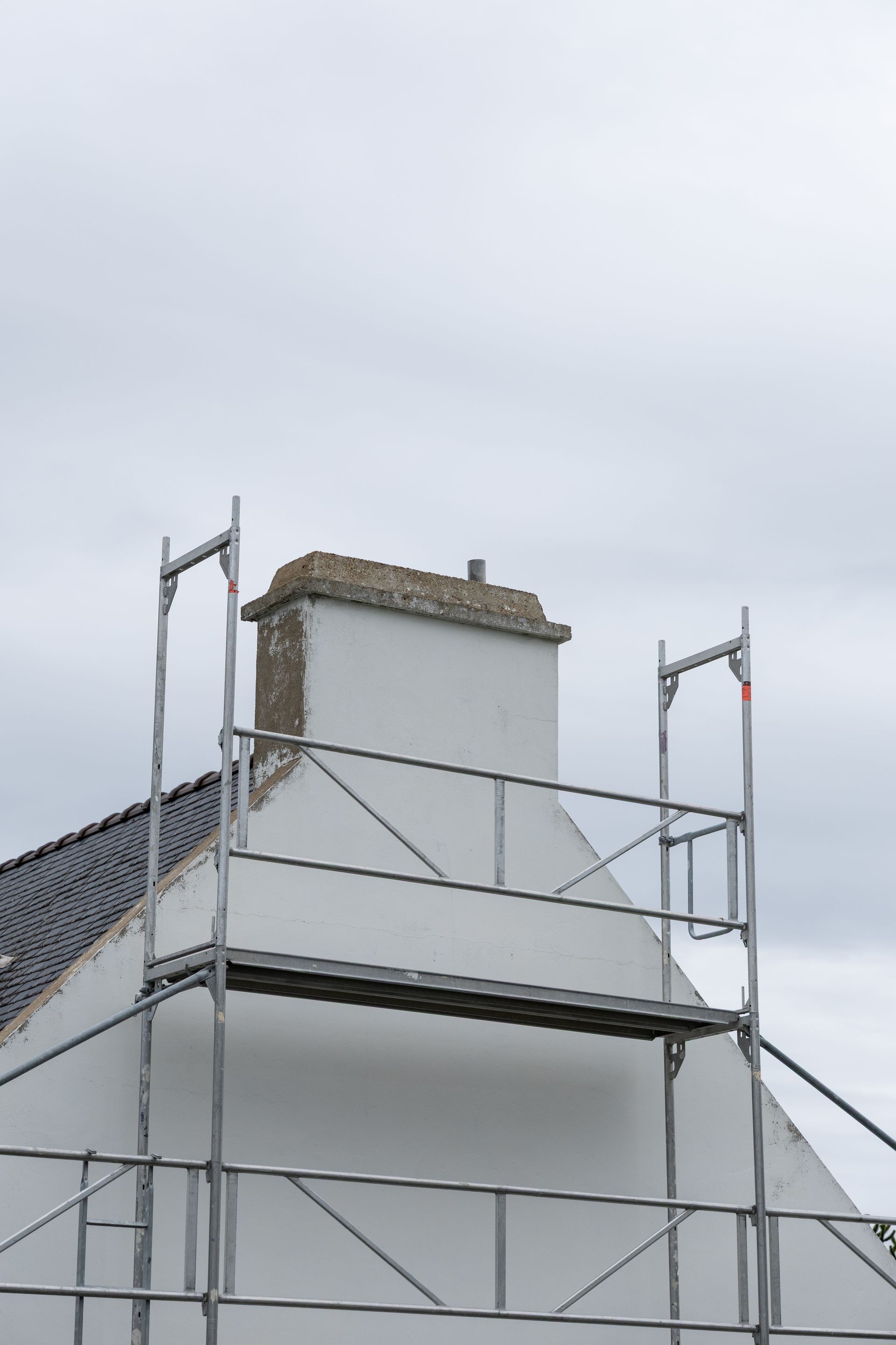 Échafaudages à côté d'une maison blanche avec une cheminée.