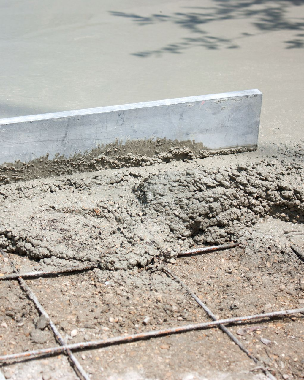 Du béton frais est nivelé à la règle sur une grille d'armature.