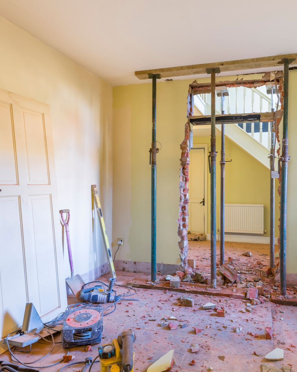 Pièce en rénovation, dépose de la porte en cours, débris au sol, poutres de soutien en place.