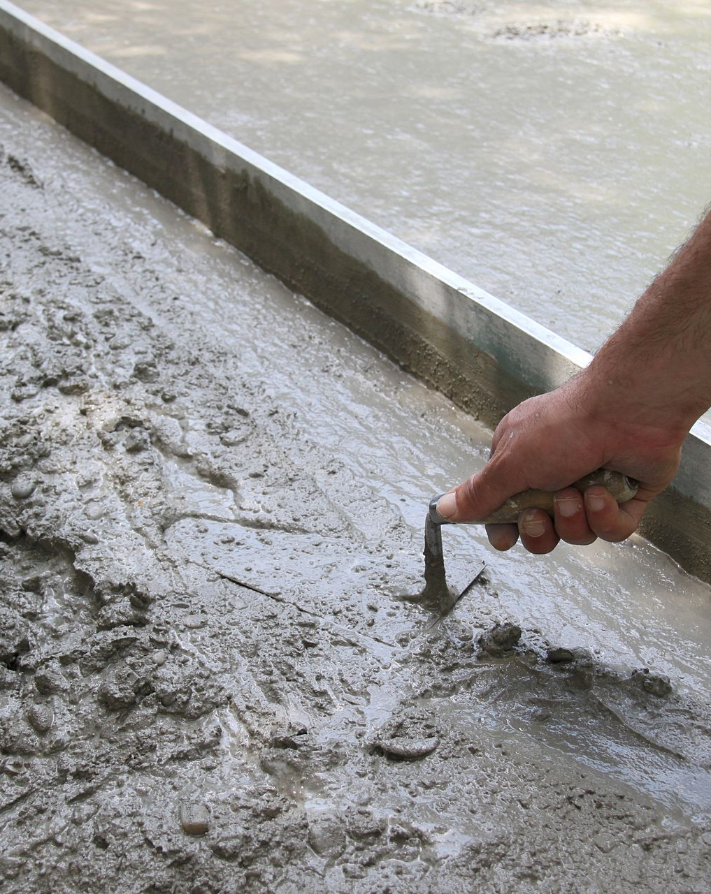 Lissage manuel du béton humide à l'aide d'une truelle, le long d'une règle métallique.