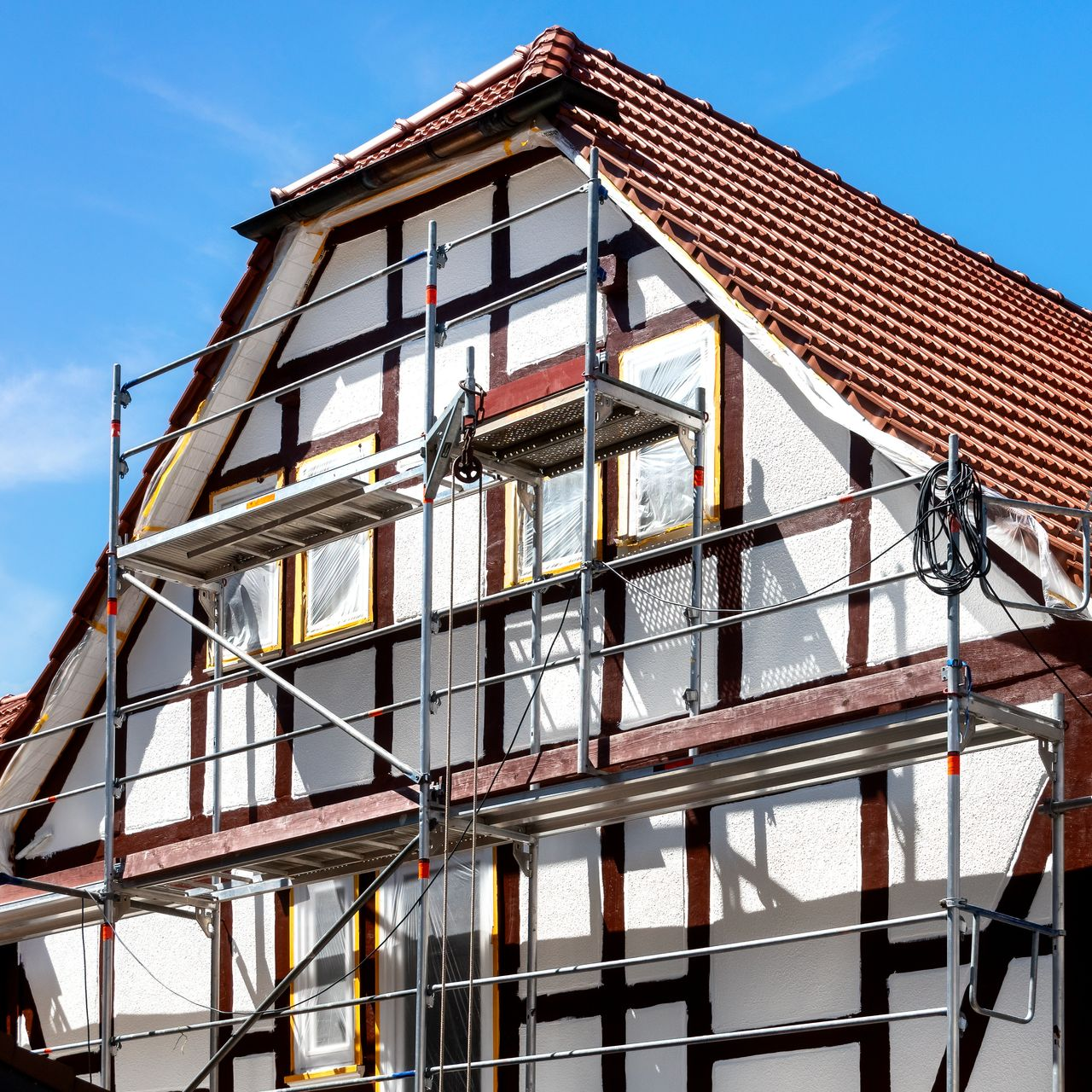 Maison au toit de tuiles rouges, poutres blanches et brunes, et échafaudages.