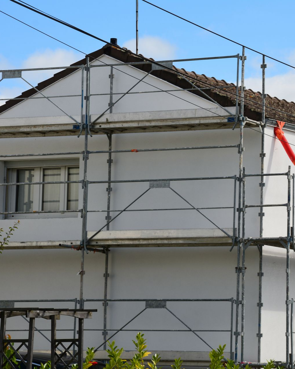 Maison blanche avec des échafaudages pour rénovation ; toit marron, ciel bleu.