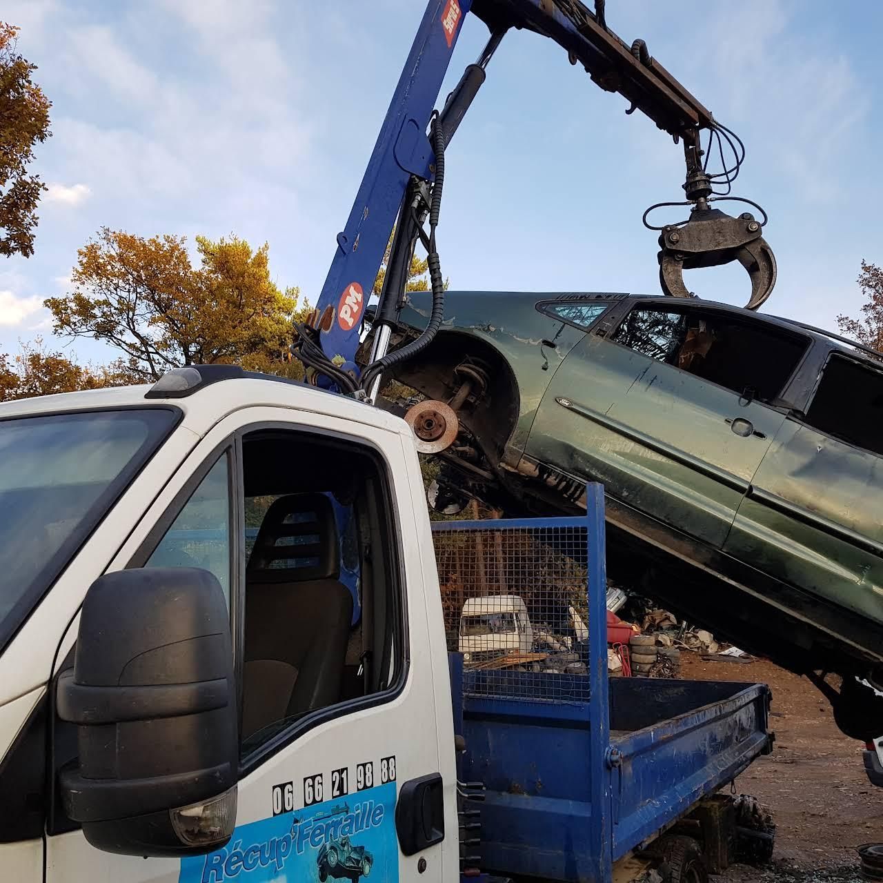 Une grue bleue soulève une voiture verte endommagée pour la déposer sur le plateau d’un camion de dépannage