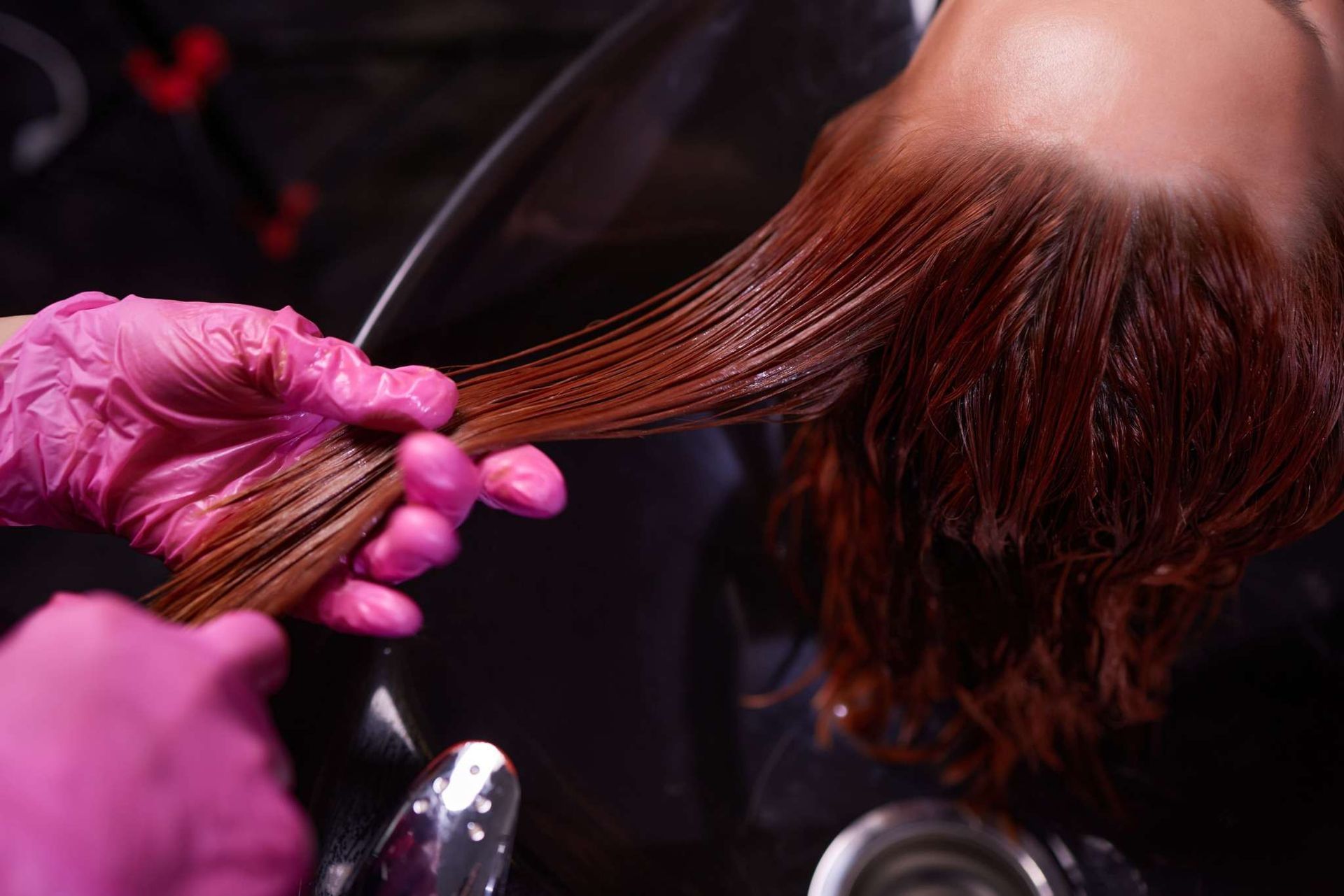 Una mano sostiene cabello mojado sobre un lavabo, mostrando cómo gotea el agua de los mechones.