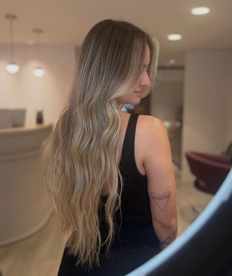 Mujer con cabello largo y ondulado, vestida con un vestido negro, de pie en un salón con iluminación tenue.