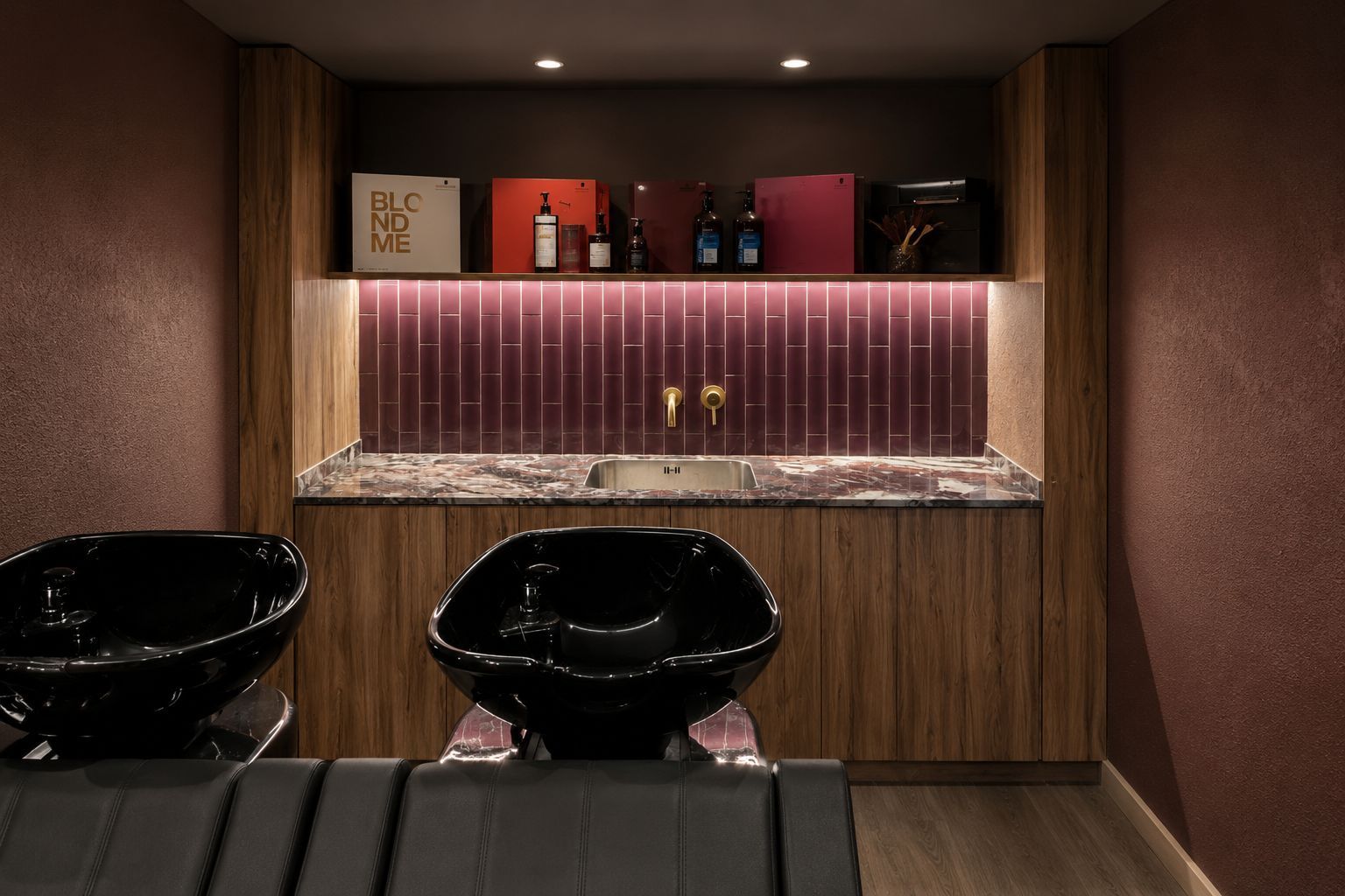 Elegante estación de lavado de cabello con dos sillones de champú negros, paneles de madera y estantes retroiluminados.