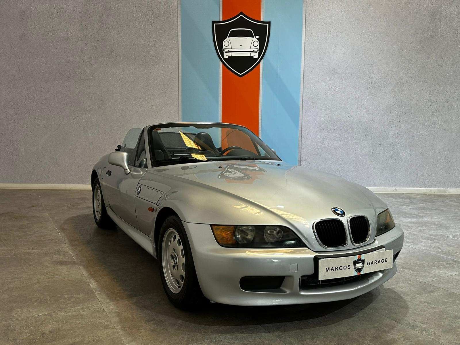 Un BMW Z3 convertible plateado está estacionado en un garaje.