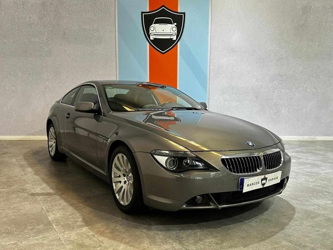 Un BMW gris está estacionado en un garaje frente a una pared con una imagen de un automóvil en ella.