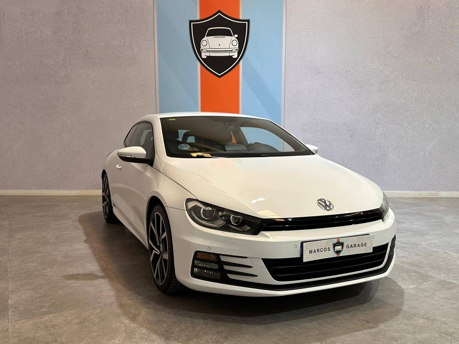 Un Volkswagen Scirocco Coupé blanco está estacionado en una sala de exposición.