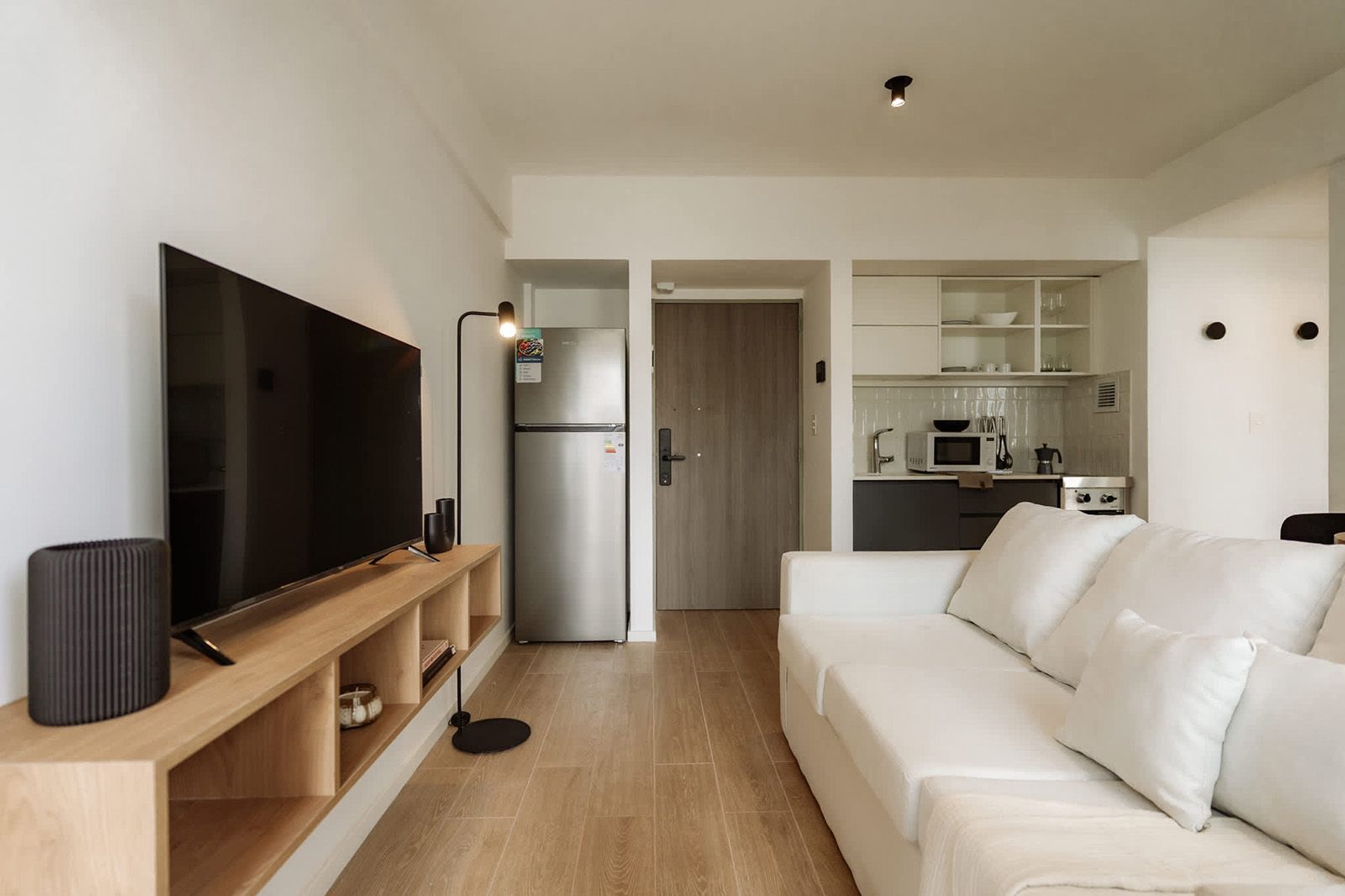 Un moderno estudio tipo apartamento que cuenta con un juego de comedor de madera, una cocina compacta con gabinetes de madera clara y pisos de madera noble.