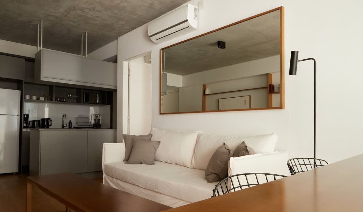Un salón de tonos neutros con un televisor montado en la pared, dos estanterías de madera, dos mesas pequeñas y sofás de color crema.