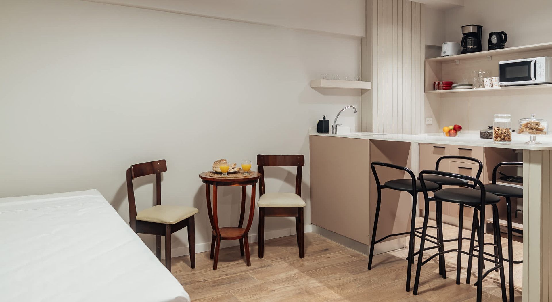 Un salón de tonos neutros con un televisor montado en la pared, dos estanterías de madera, dos mesas pequeñas y sofás de color crema.