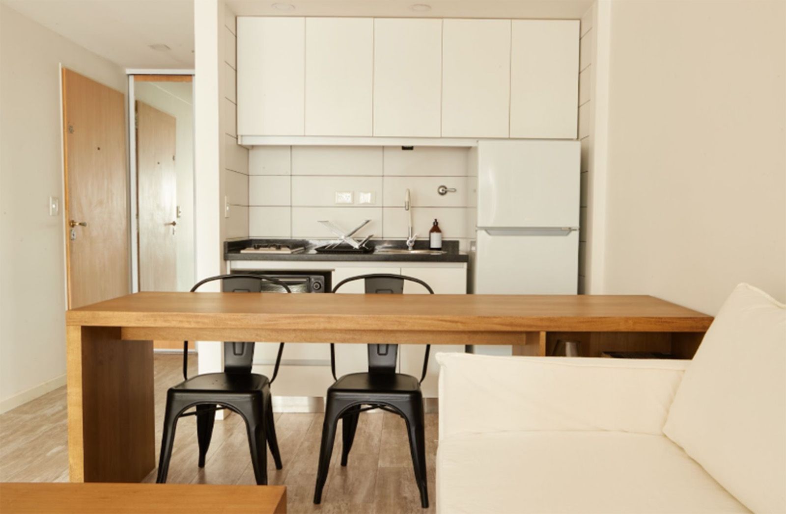 Un moderno estudio tipo apartamento que cuenta con un juego de comedor de madera, una cocina compacta con gabinetes de madera clara y pisos de madera noble.