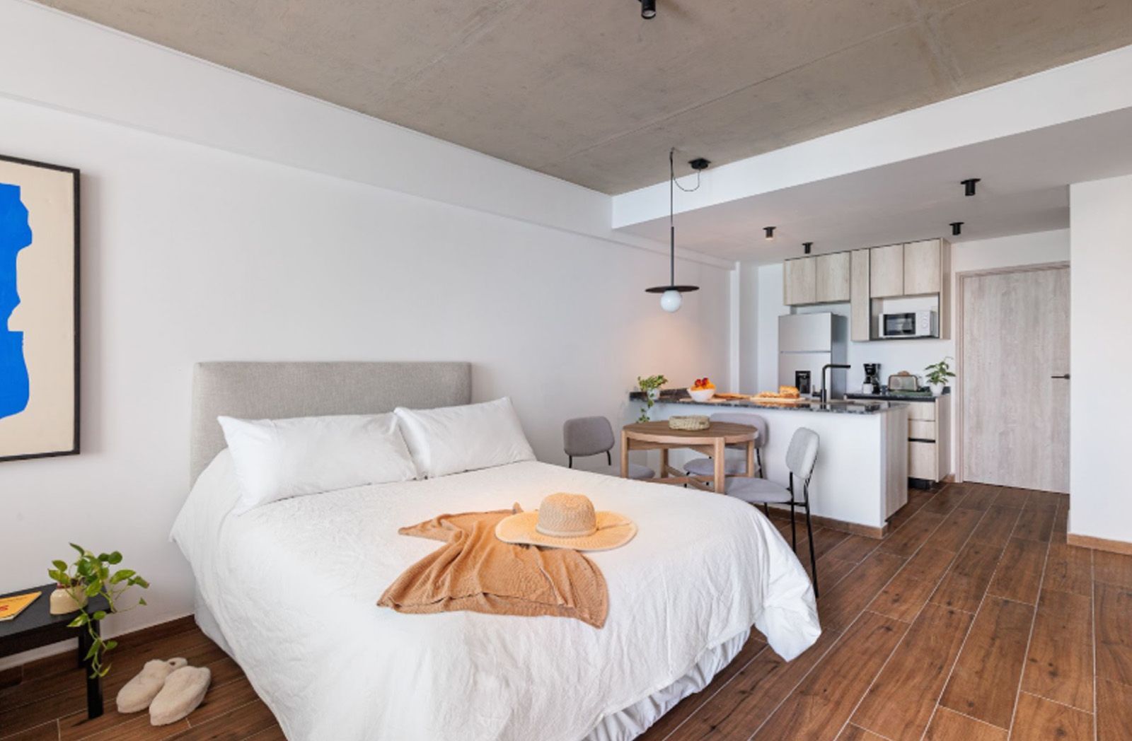 Un salón de tonos neutros con un televisor montado en la pared, dos estanterías de madera, dos mesas pequeñas y sofás de color crema.