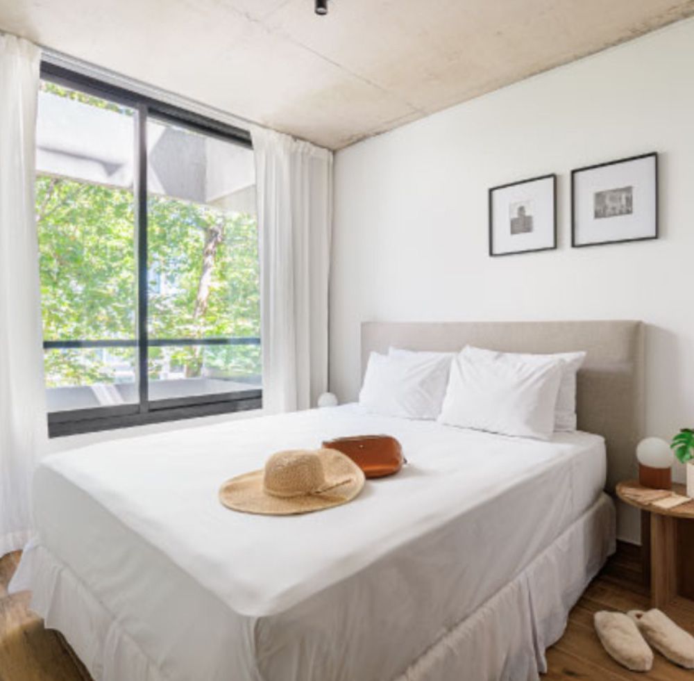 Dormitorio con cama, gran ventanal, mesa auxiliar y decoración minimalista.