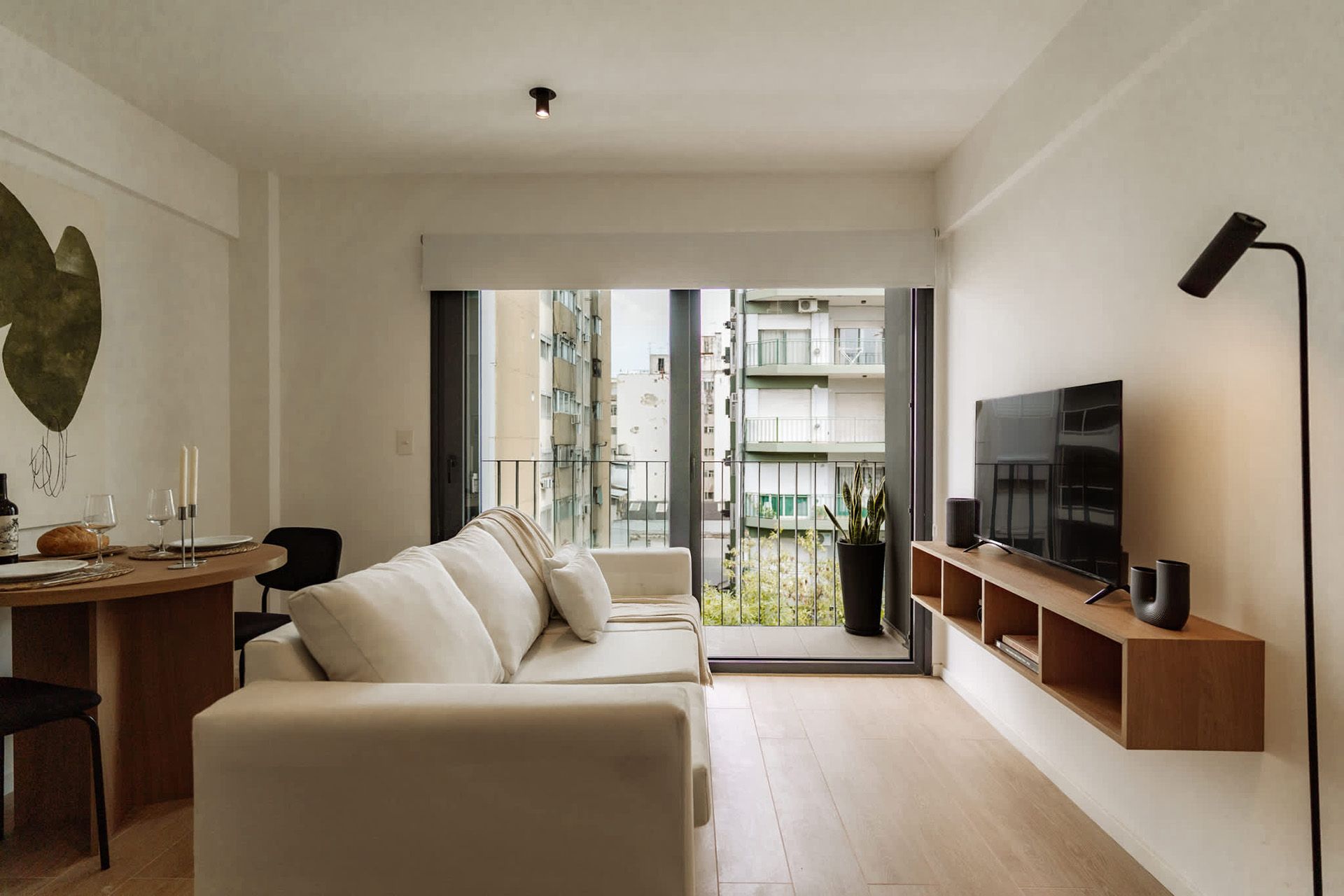 Un moderno estudio tipo apartamento que cuenta con un juego de comedor de madera, una cocina compacta con gabinetes de madera clara y pisos de madera noble.