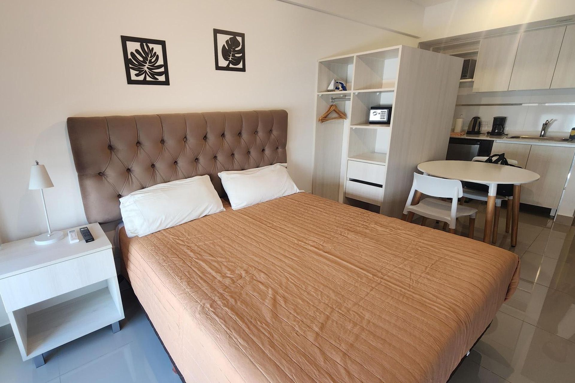 Un salón de tonos neutros con un televisor montado en la pared, dos estanterías de madera, dos mesas pequeñas y sofás de color crema.