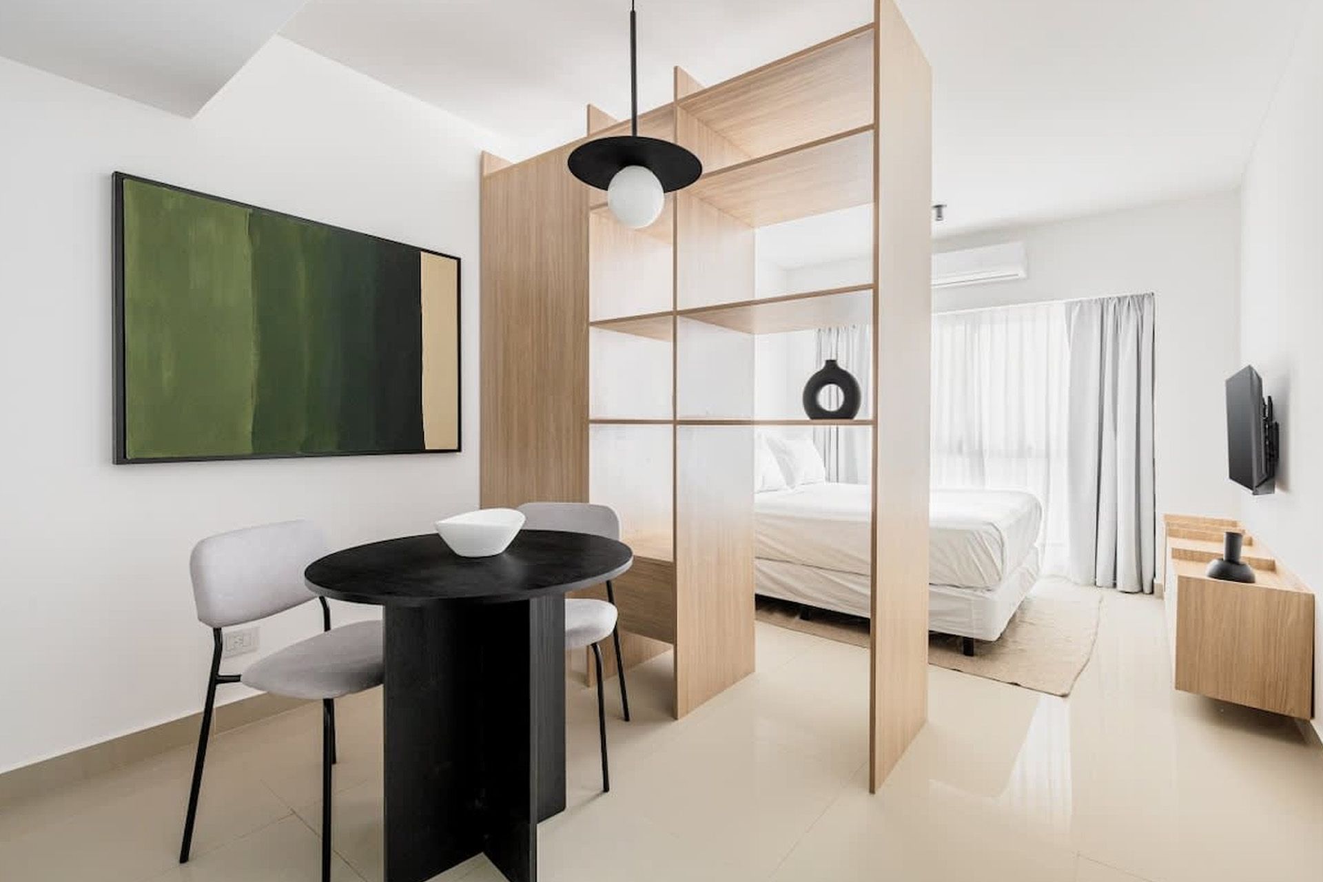 Un salón de tonos neutros con un televisor montado en la pared, dos estanterías de madera, dos mesas pequeñas y sofás de color crema.
