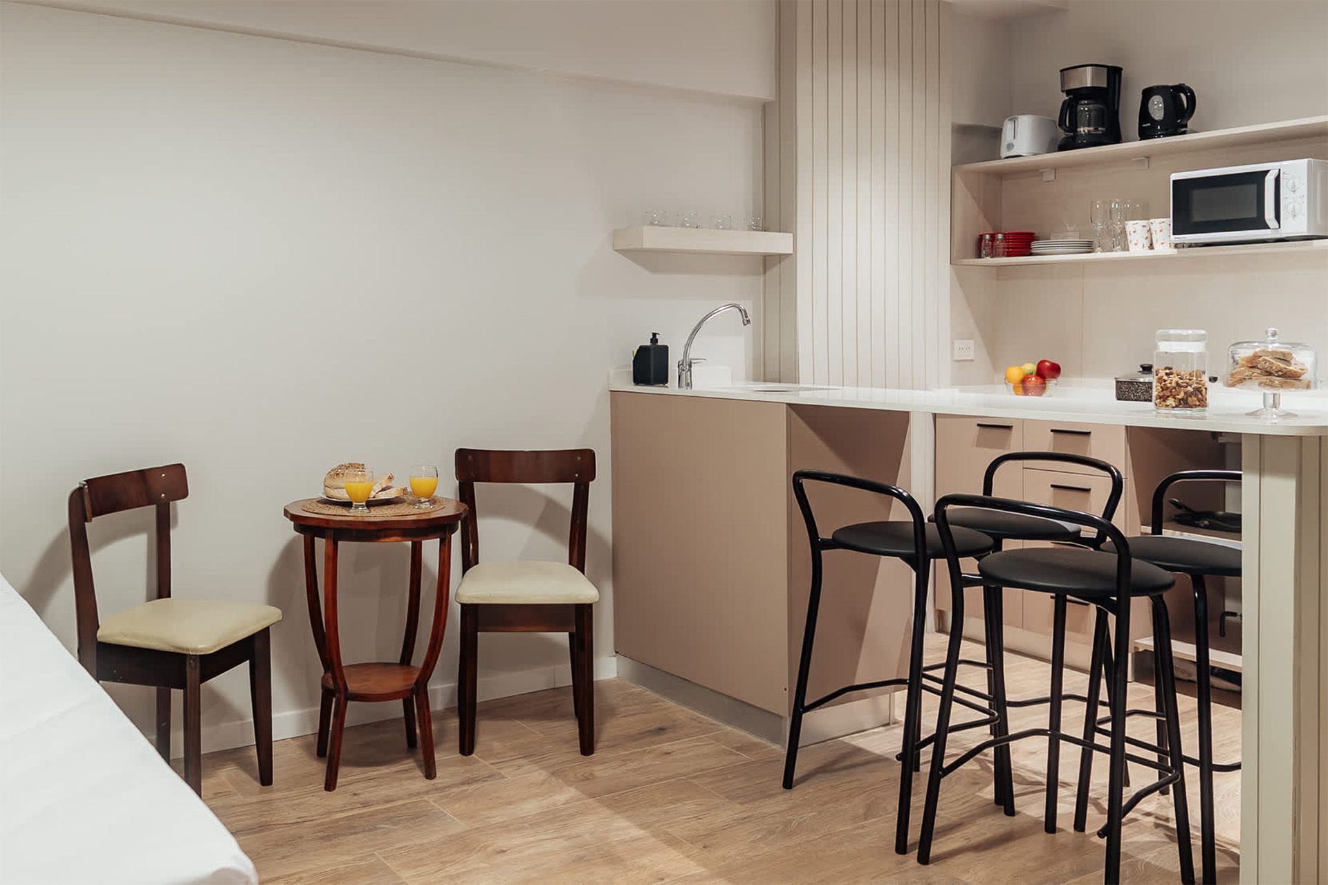 Un salón de tonos neutros con un televisor montado en la pared, dos estanterías de madera, dos mesas pequeñas y sofás de color crema.
