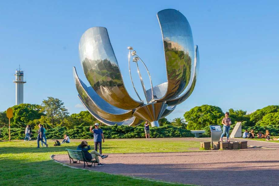 Recoleta La Floralis Genérica, una gran escultura metálica en forma de flor, se encuentra en un soleado parque de Buenos Aires, rodeada de gente que pasea.