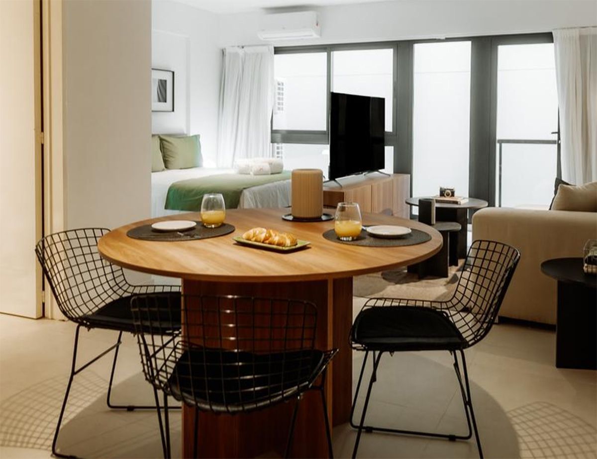 Camino a través de un jardín de rosas con gente sentada en bancos. Rosas rosas y rojas, árboles y un cielo azul.