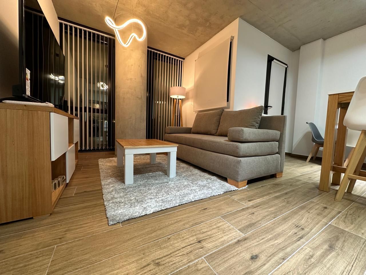 Sala de estar con paredes blancas, TV, muebles de madera y un sofá.