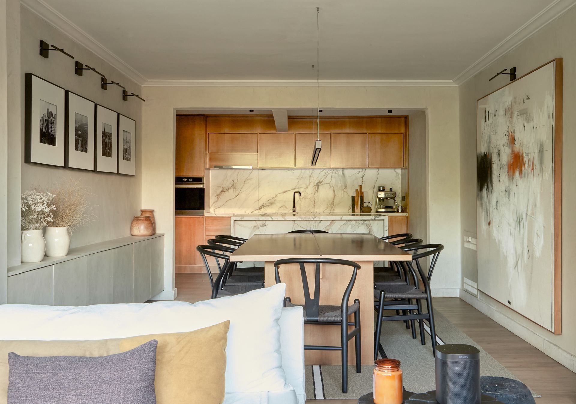 Comedor con mesa y sillas de madera, conectado a una cocina revestida de madera. Gran obra de arte en la pared.