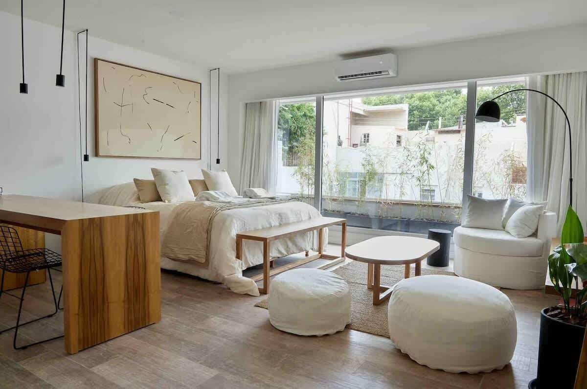 Un moderno estudio tipo apartamento que cuenta con un juego de comedor de madera, una cocina compacta con gabinetes de madera clara y pisos de madera noble.