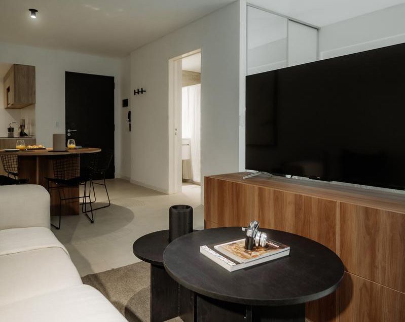 Un moderno estudio tipo apartamento que cuenta con un juego de comedor de madera, una cocina compacta con gabinetes de madera clara y pisos de madera noble.