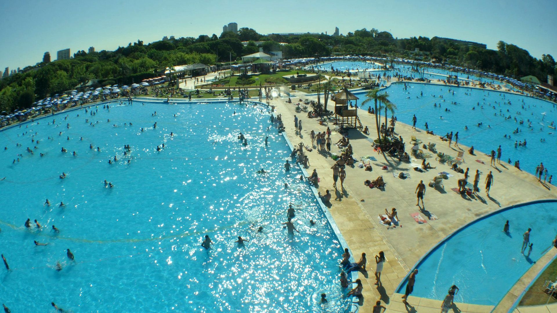 Un puente blanco sobre un lago con un barco. Está rodeado de árboles y césped verde.