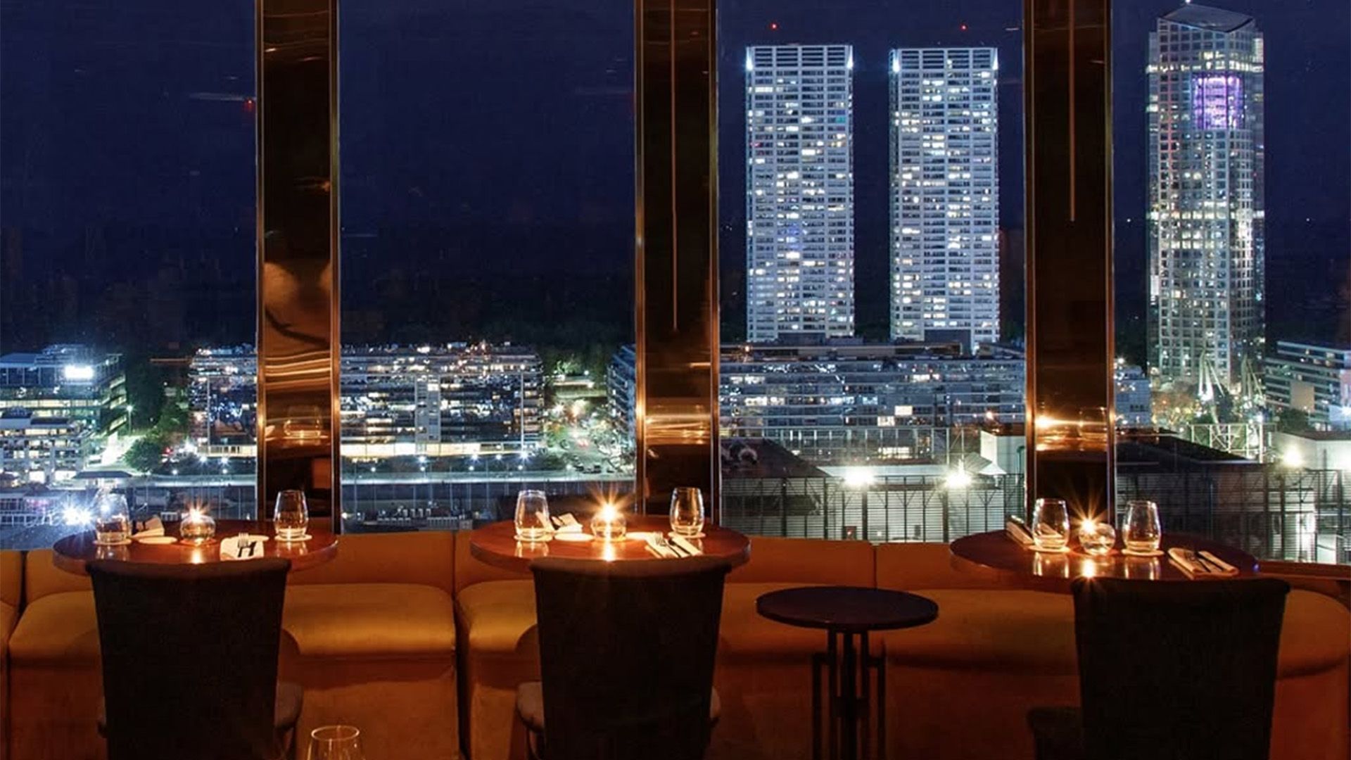 Vista aérea de un parque con un lago, árboles, senderos y un edificio blanco. Hay carreteras que bordean el parque.