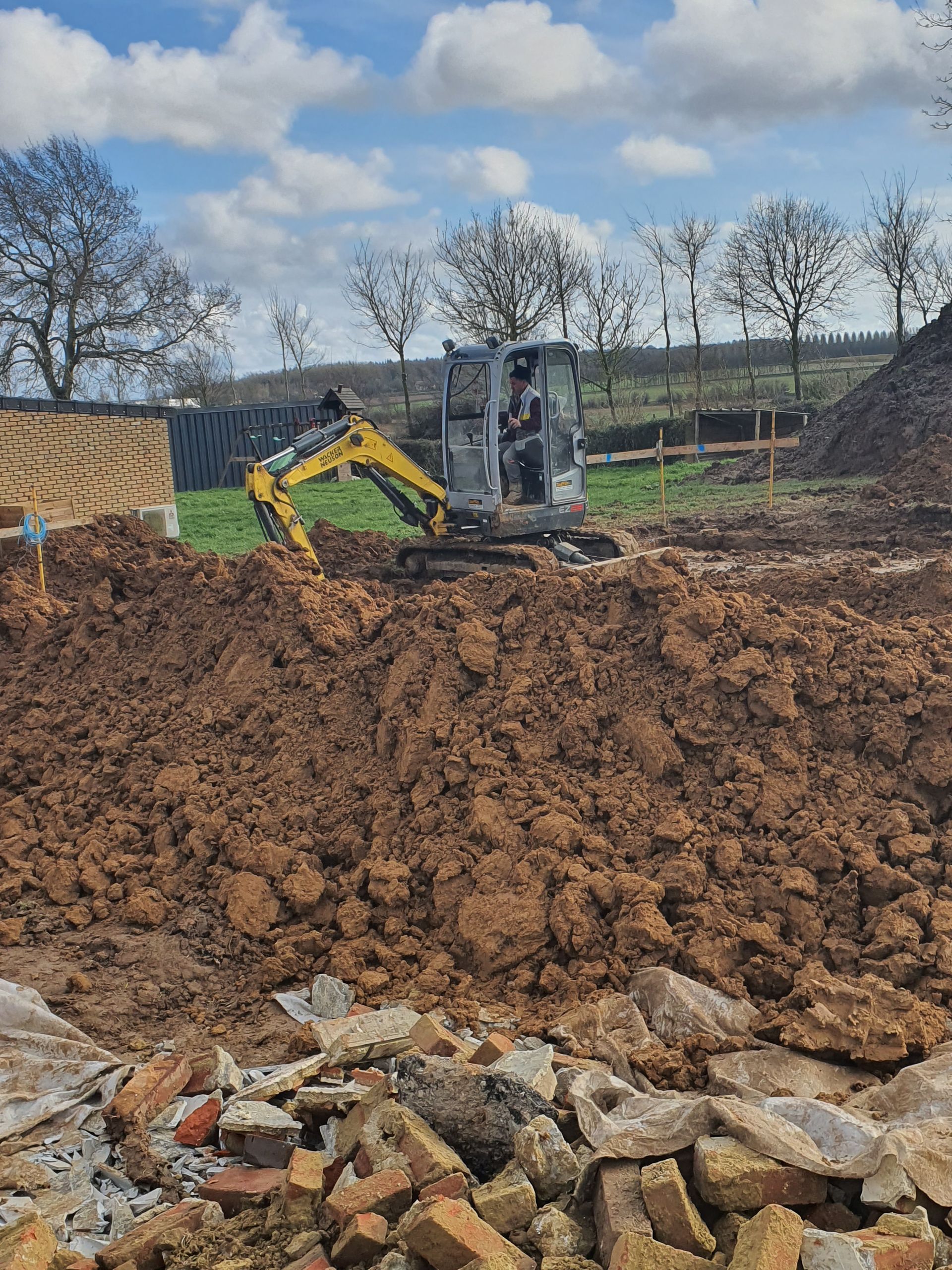Une mini-pelle creuse la terre sur un chantier de construction par une journée ensoleillée.