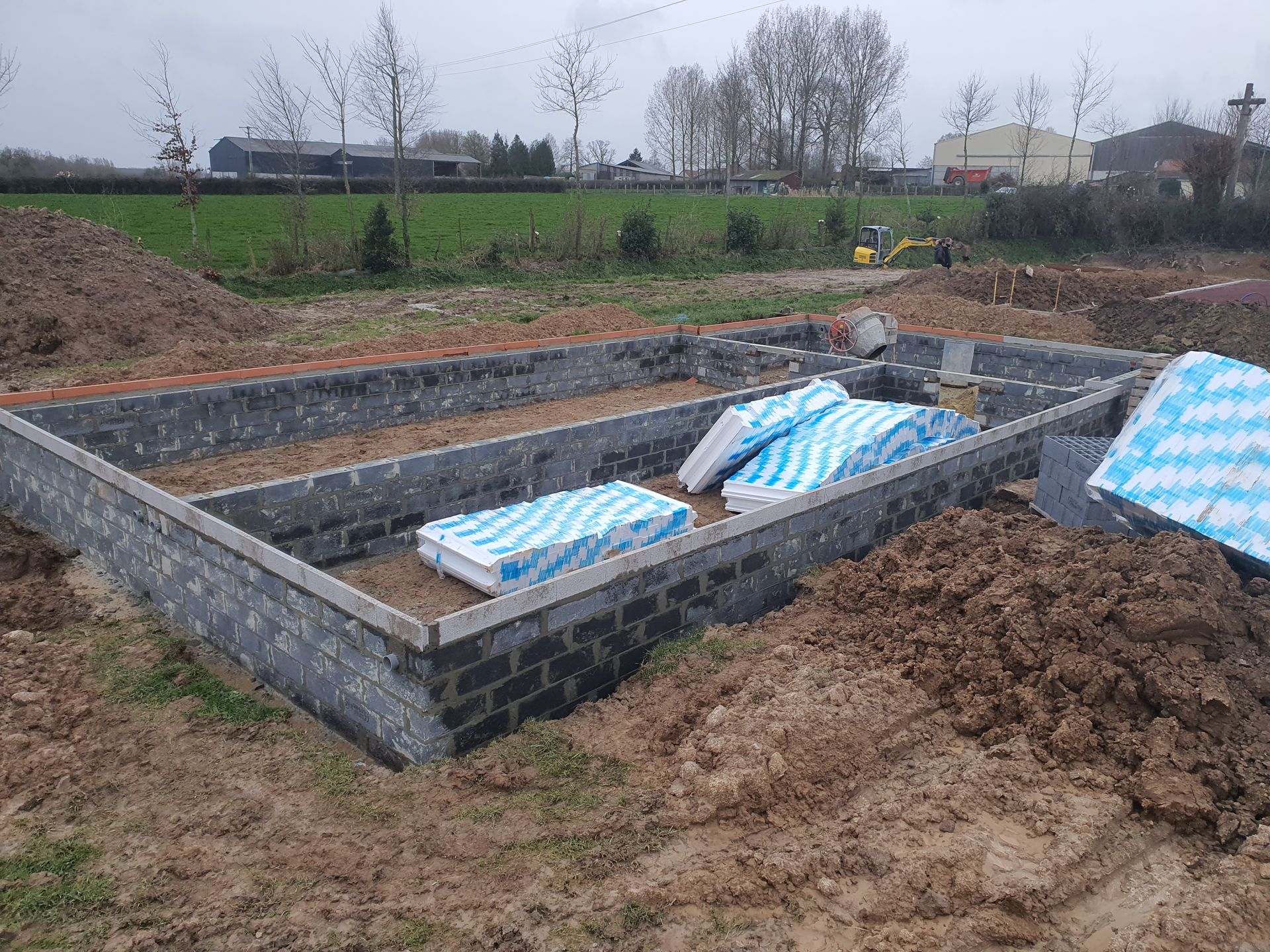 Fondations d'un bâtiment en construction, avec murs en parpaings et panneaux isolants.