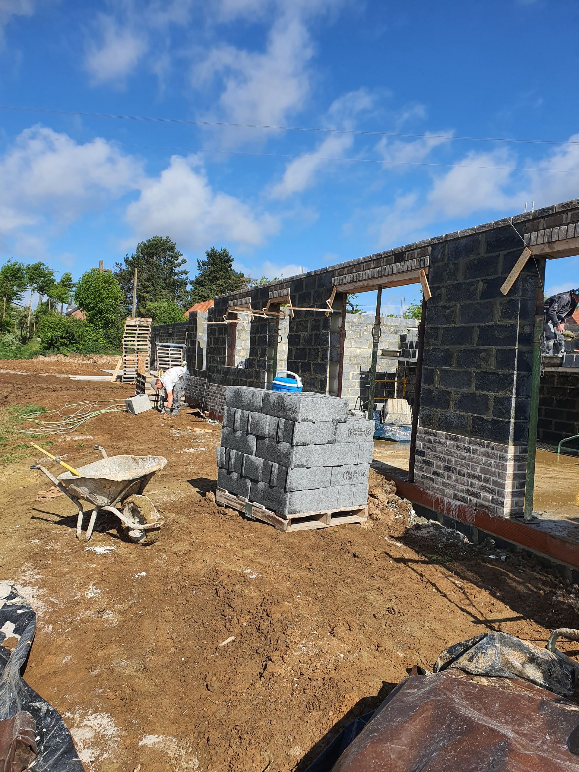 Chantier de construction avec une structure en pierre partiellement édifiée, une brouette