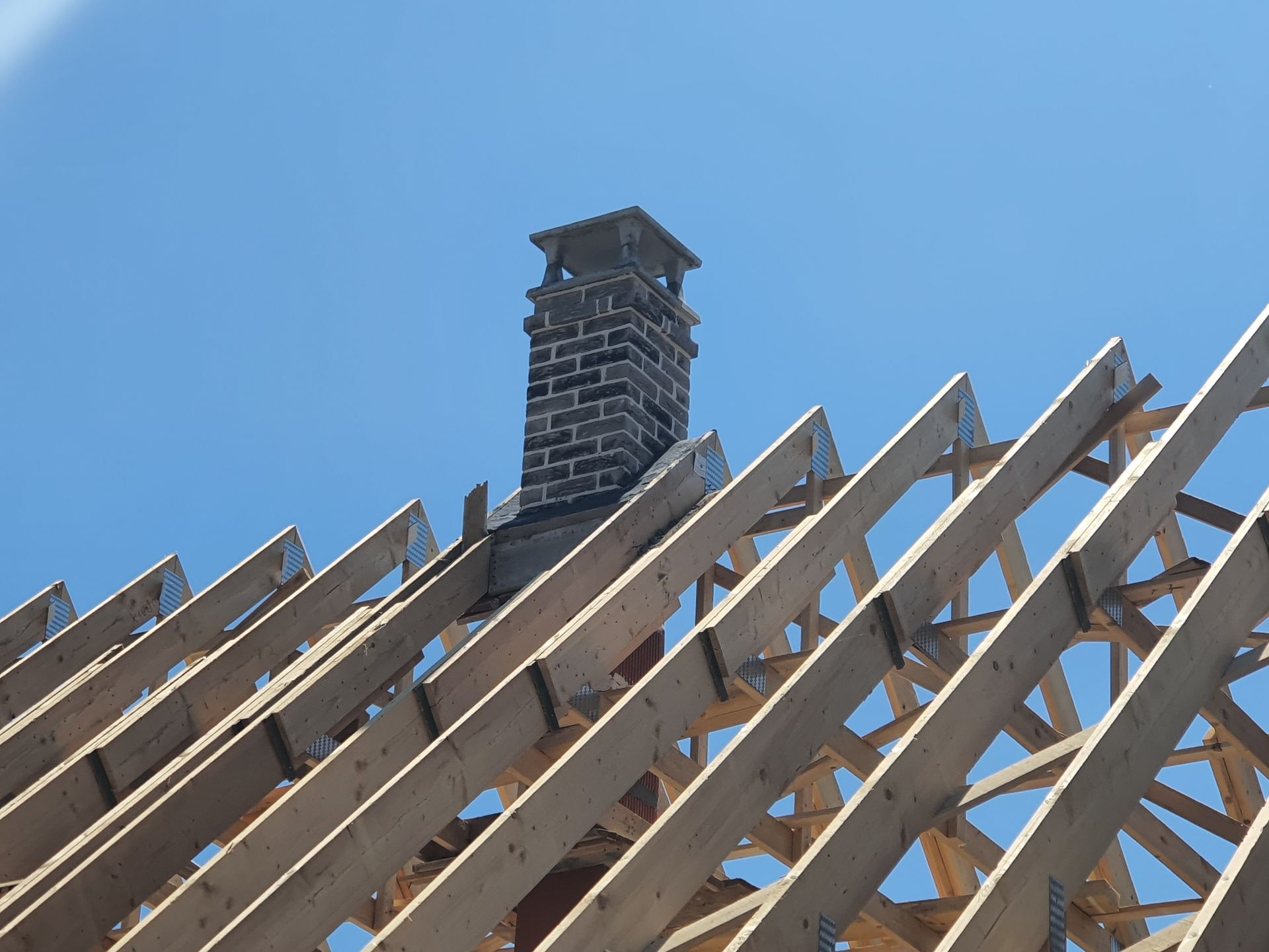 Charpente de toit en bois avec une cheminée en briques se détachant sur un ciel bleu éclatant.
