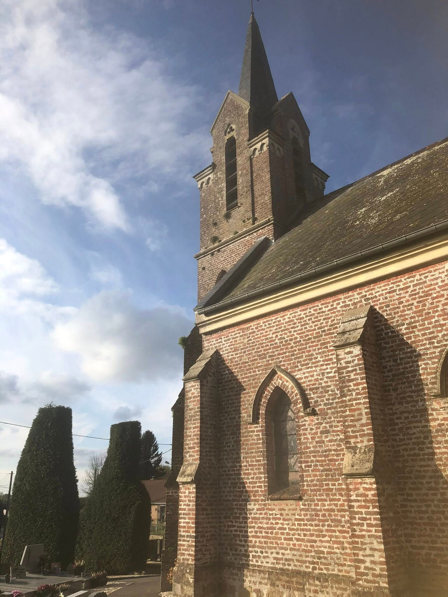 Église en briques avec un haut clocher se détachant sur un ciel bleu partiellement nuageux.
