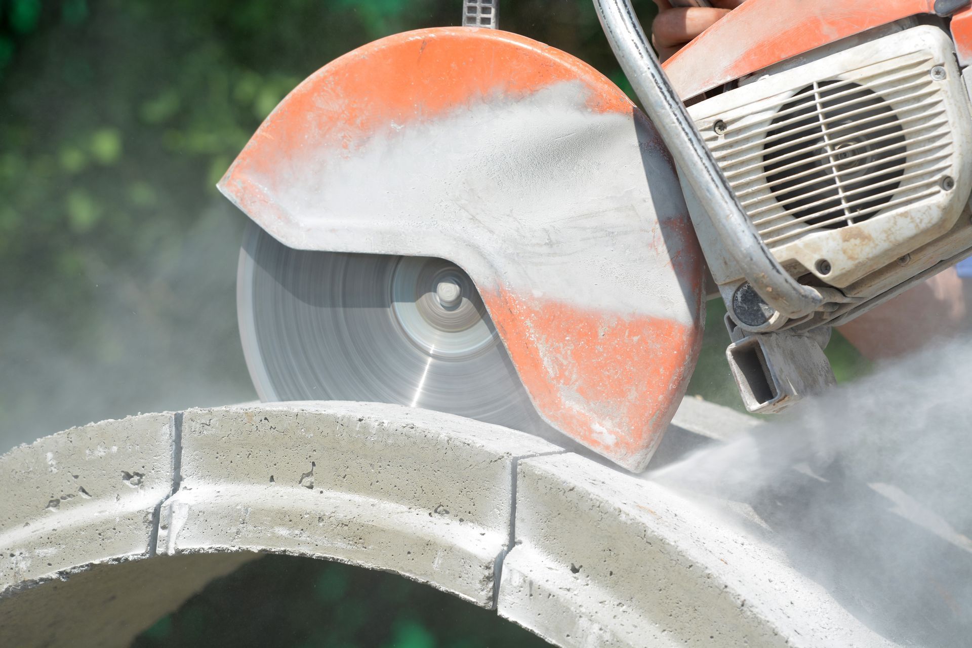 Une scie circulaire découpe un anneau de béton, créant de la poussière.