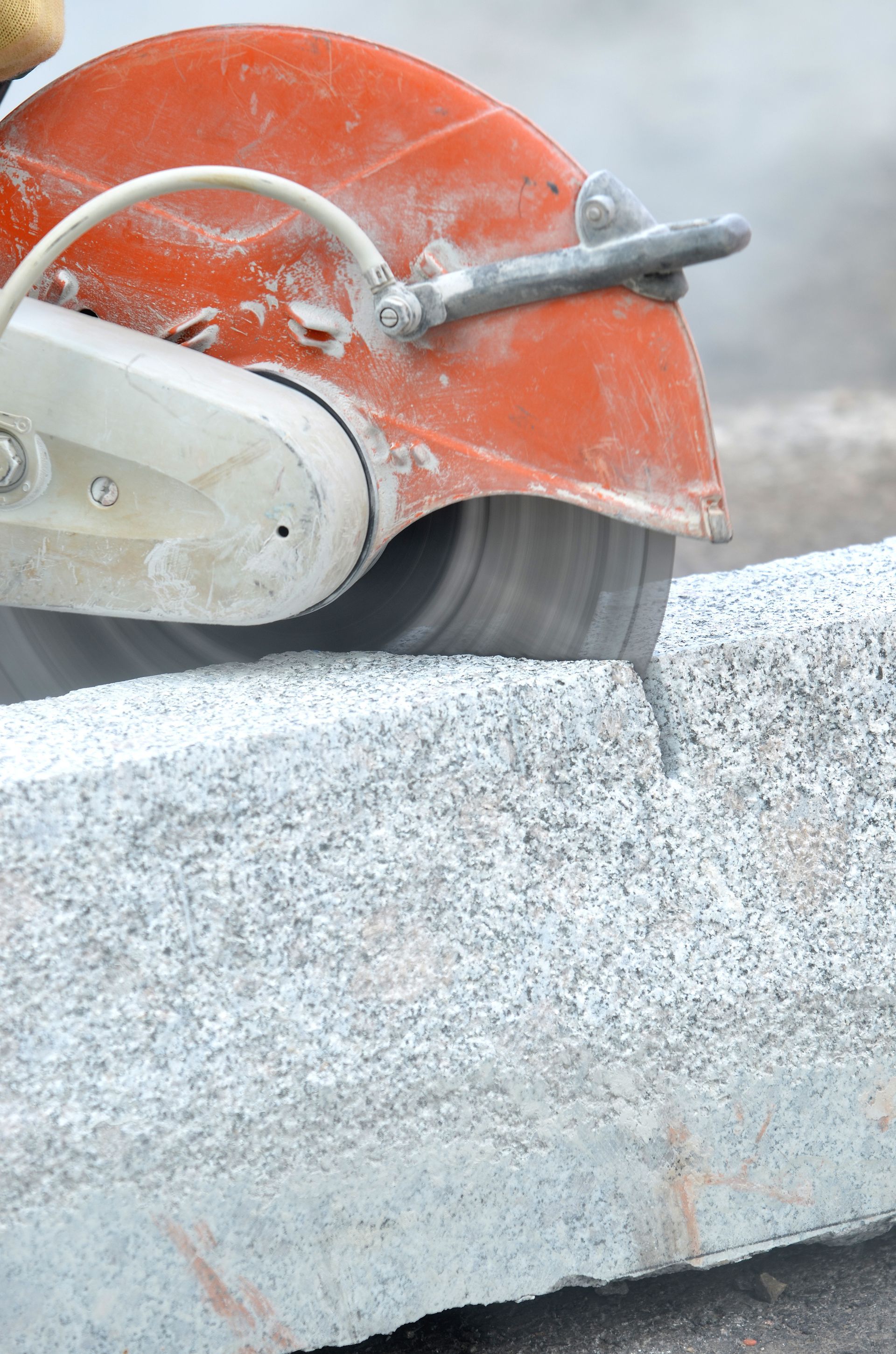 Une scie orange trace une ligne sur un bloc de pierre grise.