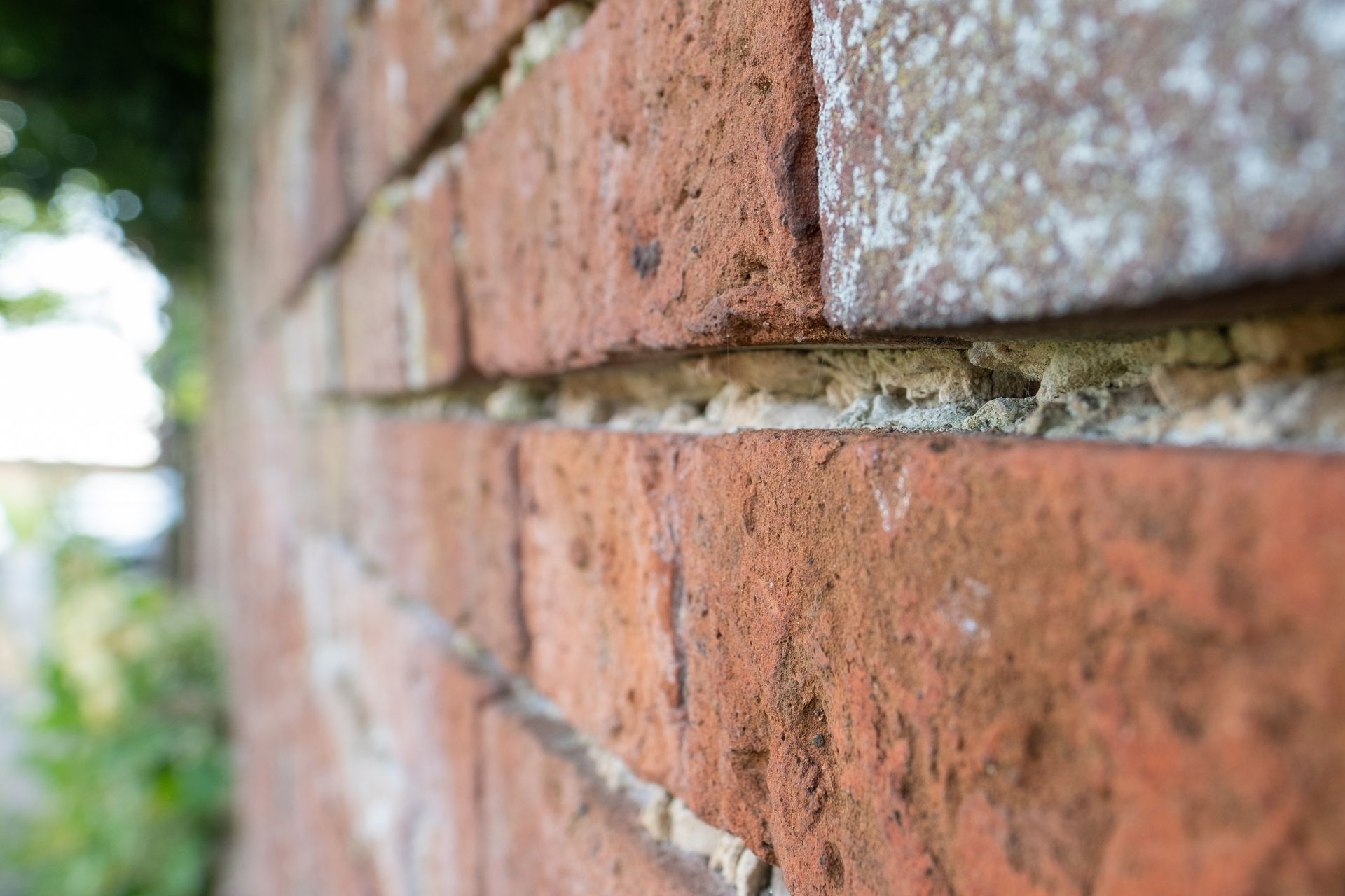 Gros plan sur un mur de briques rouges patiné par le temps, avec un mortier blanc, vue en biais.