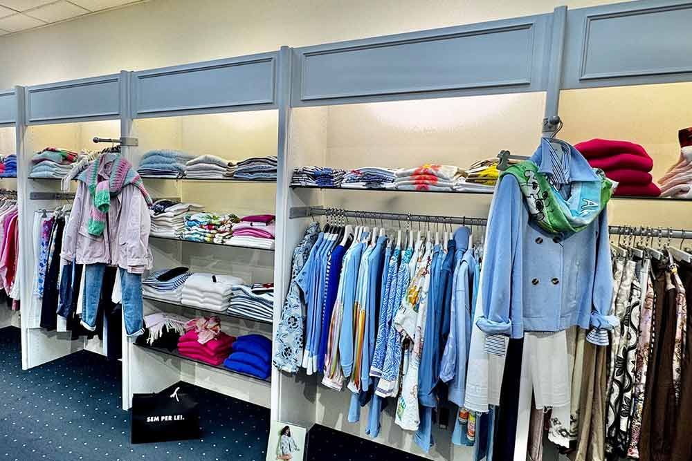 Innenansicht eines Bekleidungsgeschäfts mit Kleiderständern und Regalen, auf denen verschiedene Kleidungsstücke in Blau und anderen Farben ausgestellt sind.