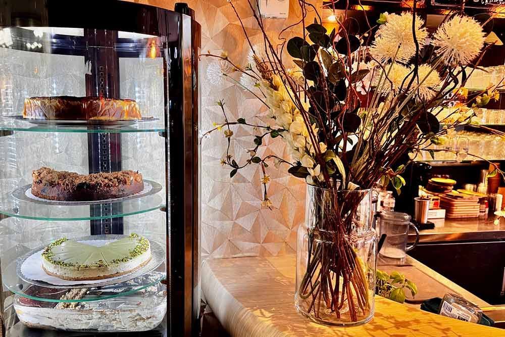 Kuchen in einer Glasvitrine neben einer Blumenvase auf einer Theke in einem Café.
