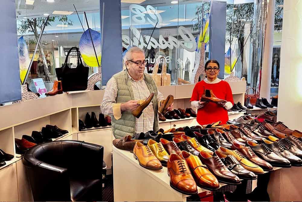 Zwei Personen in einem Schuhgeschäft, die verschiedene Lederschuhe ausstellen. Der Mann hält einen Schuh, die Frau einen roten.