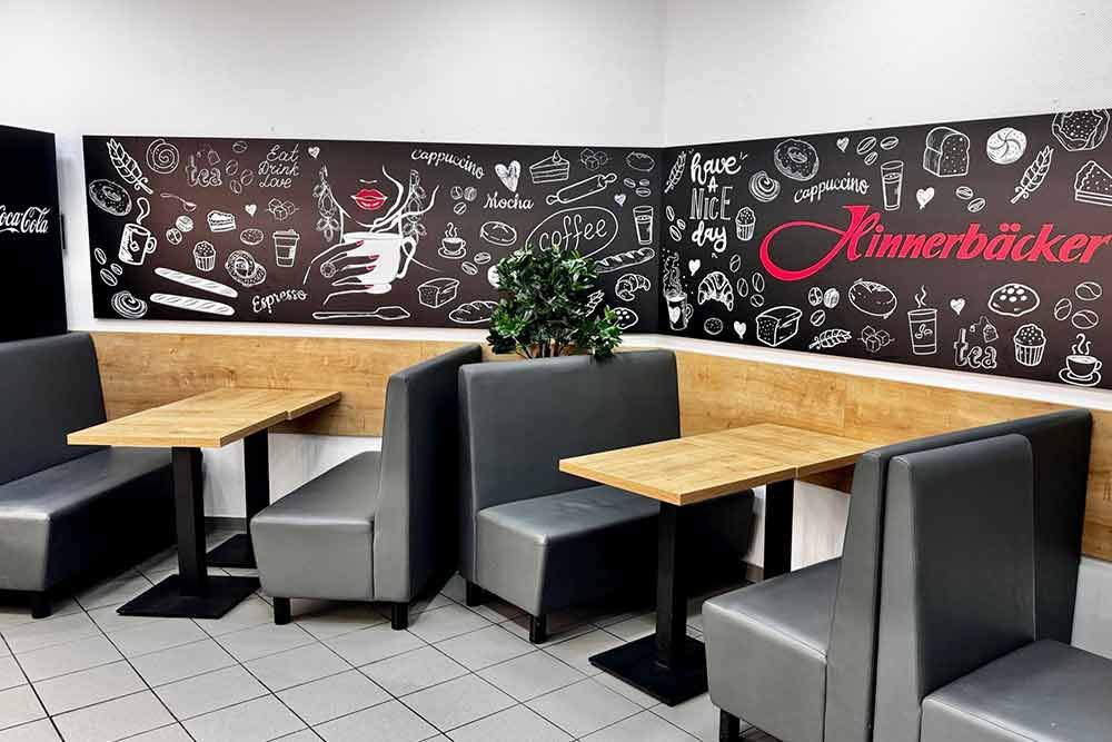 Ecksitznischen in einem Café mit schwarzer Kreidetafel-Wandkunst, kleinen Tischen und grauen Polstermöbeln.