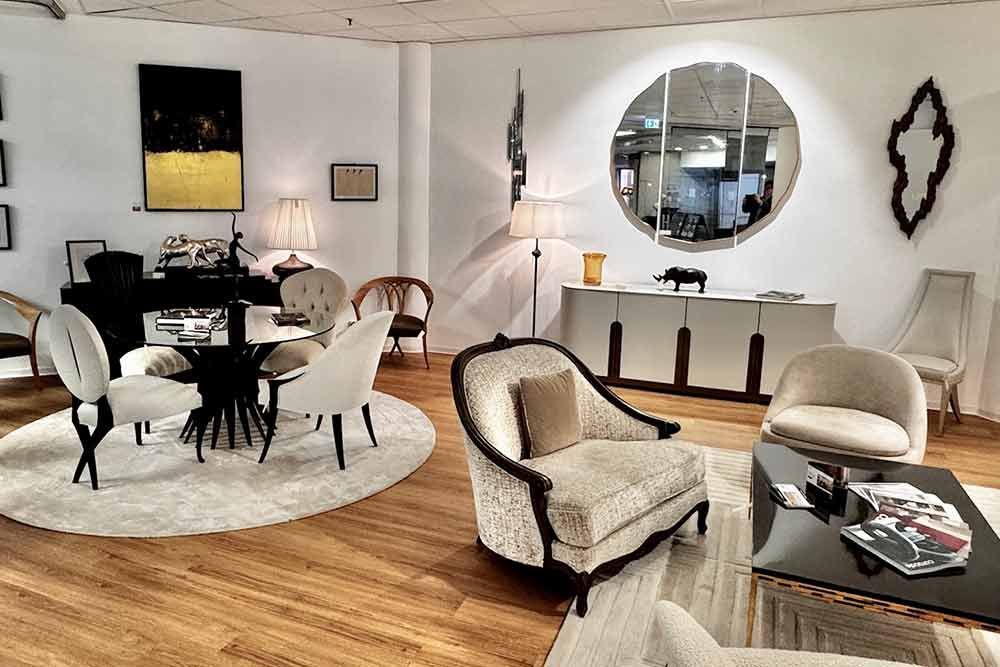 Ein Ausstellungsraum für Inneneinrichtung mit verschiedenen Möbelstücken, darunter Stühle, Tische und ein großer runder Spiegel.