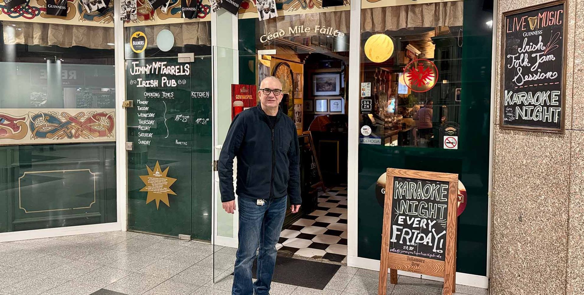 Ein Mann steht vor dem Eingang eines Restaurants. Der Eingang hat grüne Türen und ein Kreidetafel-Schild.