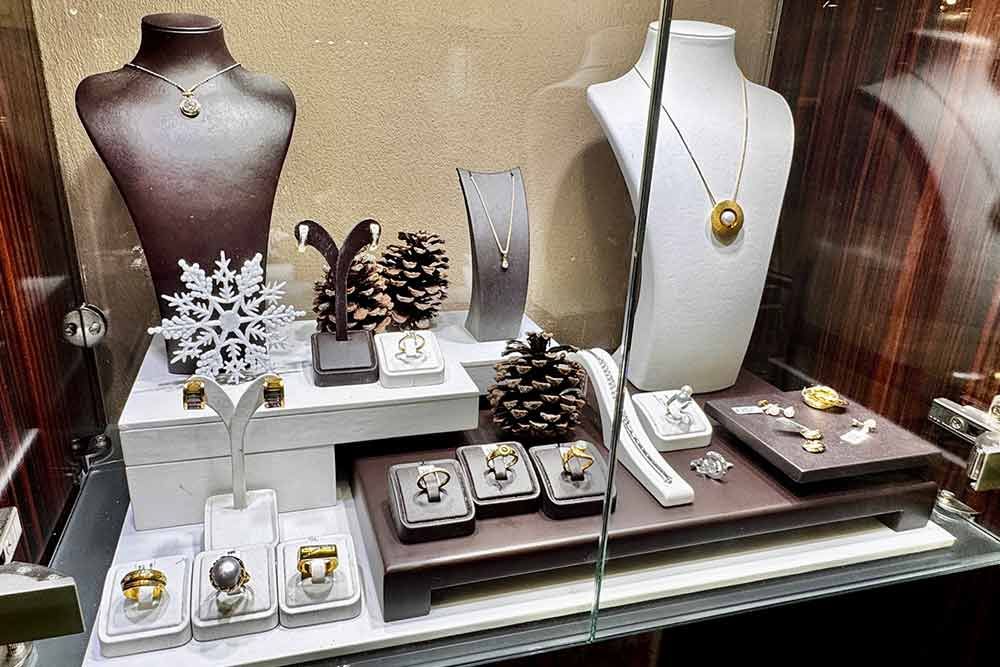 Schmuckvitrine mit Halsketten, Ringen und Ohrringen auf Büsten und Podesten; Braun-, Weiß- und Goldtöne.