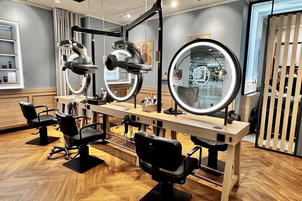 Interieur eines Friseursalons mit drei Frisierplätzen. Jeder Platz ist mit einem Stuhl, einem Spiegel mit Ringlicht und einem Haartrockner ausgestattet.