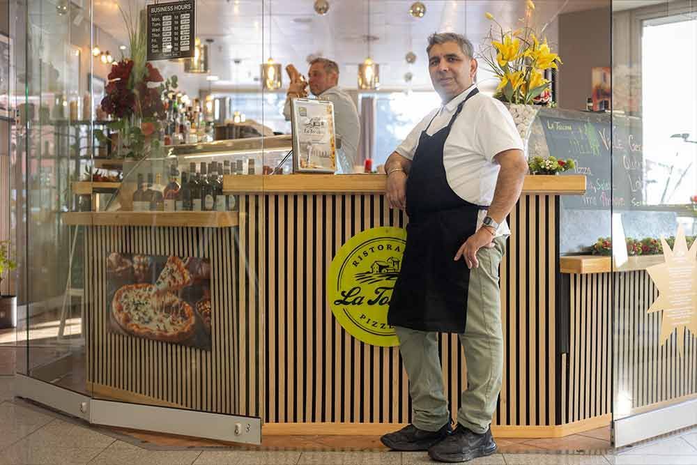 Ein Mann in Schürze steht am Tresen des Restaurants „La Forchetta“, im Hintergrund ist ein weiterer Angestellter zu sehen.